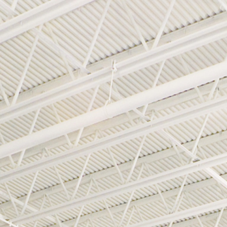 Interior view of a white metal building ceiling with exposed steel beams and open-web trusses supporting ribbed roof decking.